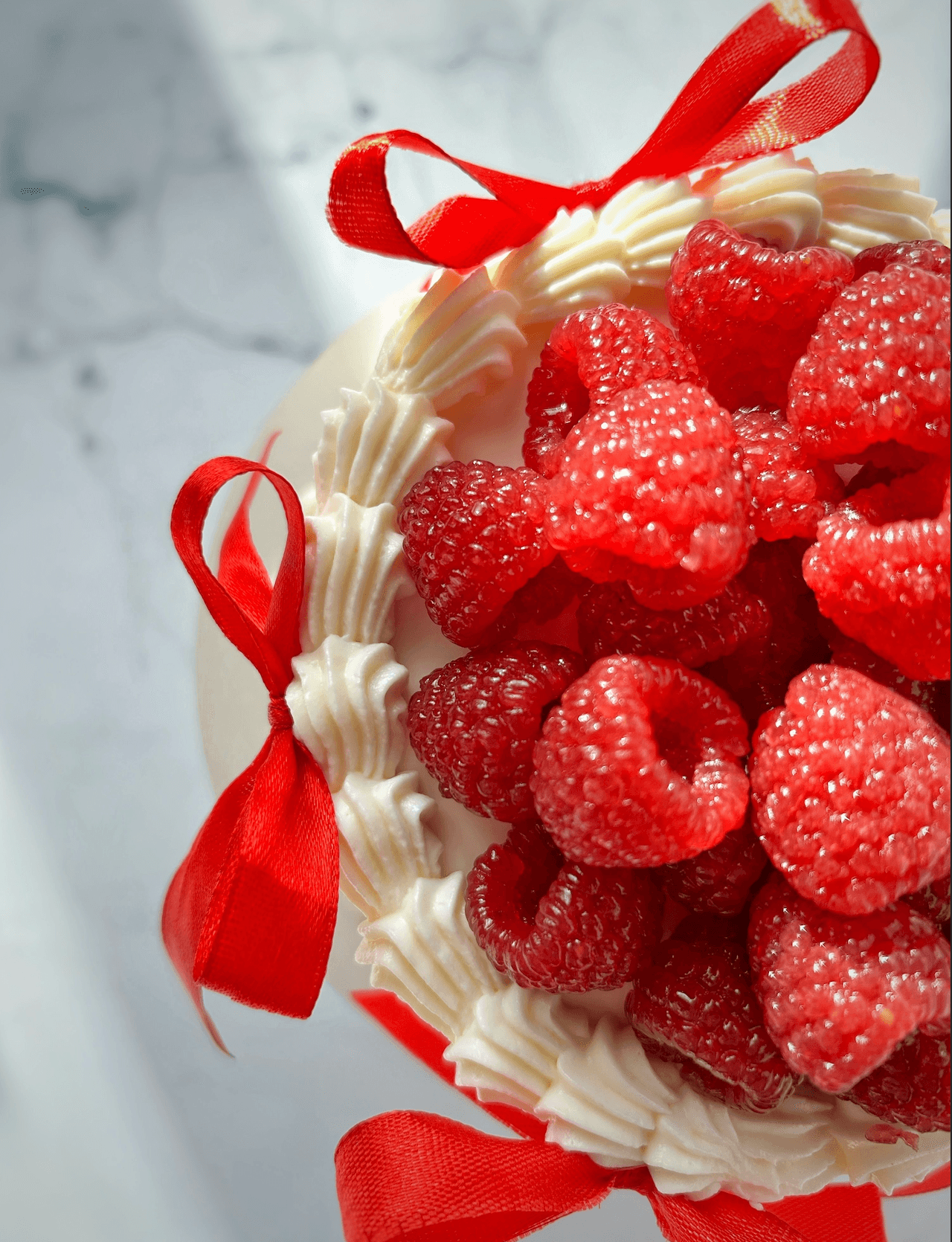 Torta sa umućenim šlagom ukrašena svežim malinama i crvenom trakom